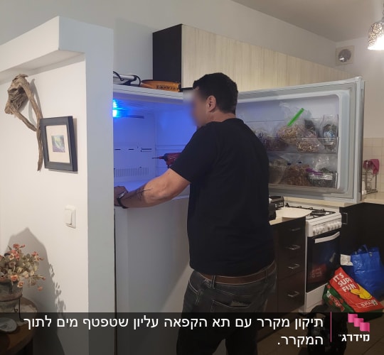 אדם עובד על מקרר פתוח במטבח ביתי
